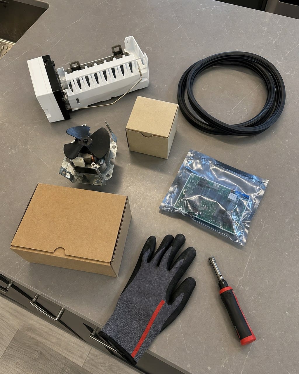 Flat-lay of genuine OEM Sub-Zero parts — ice-maker module, door gasket, fan motor and control board